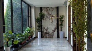 Un pasillo moderno con amplias ventanas, plantas en macetas y una pared de mármol.