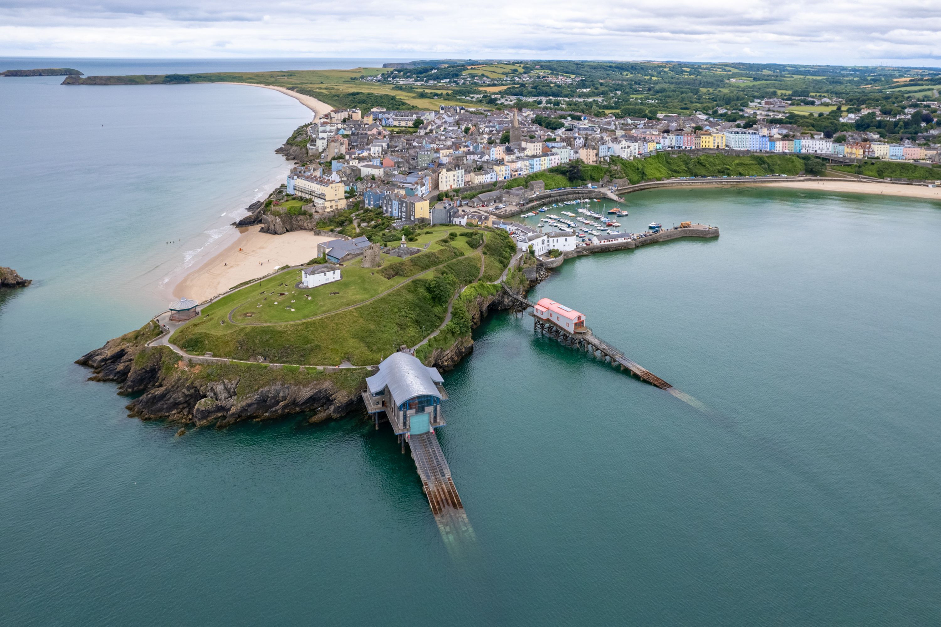 An aerial view of a coastal town with a prominent pier, a sandy beach, and a marina.