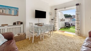 Un salon comprenant une table à manger, des chaises, un téléviseur et donnant sur un jardin.