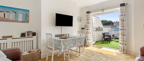 A living room with a dining table, chairs, a TV, and a view of a garden.