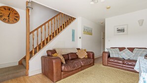 Un salon avec un escalier en bois, deux canapés en cuir, une grande horloge et un tapis moelleux.