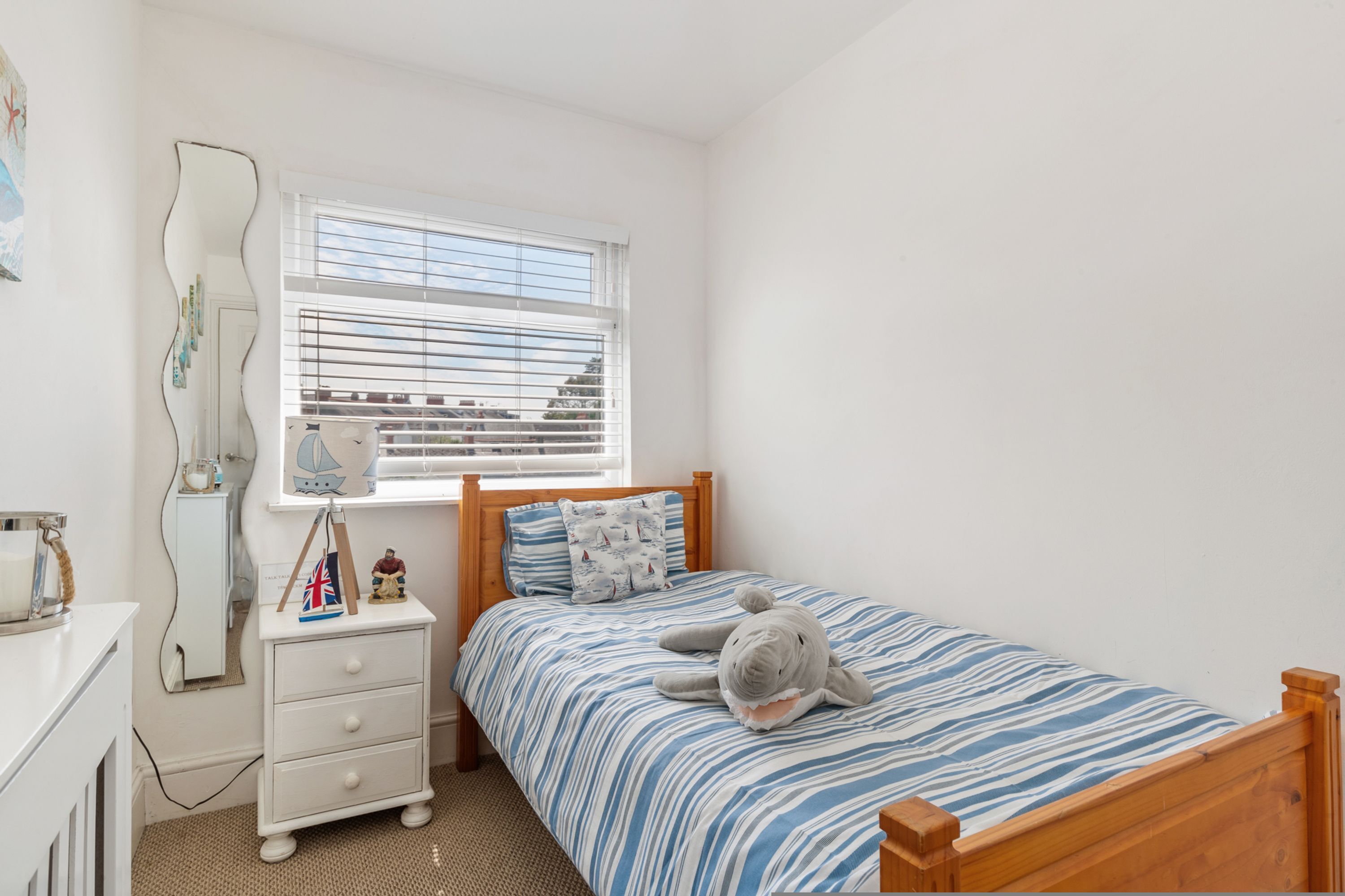 Une chambre à coucher avec un lit, une table de chevet, un miroir et une fenêtre avec des stores.