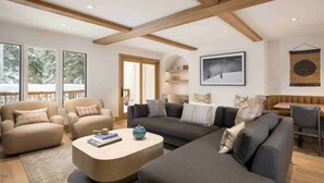 A spacious living room with a large sofa, armchairs, and a coffee table. There is a dining area with a wooden table and chairs. The room has large windows and a view of the outdoors. - Vail Village Luxury 4 Bedroom, Steps to Slopes! (Vail)