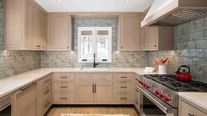A kitchen with wooden cabinets, a gas stove, and a window with a view of trees. - Vail Village Luxury 4 Bedroom, Steps to Slopes! (Vail)