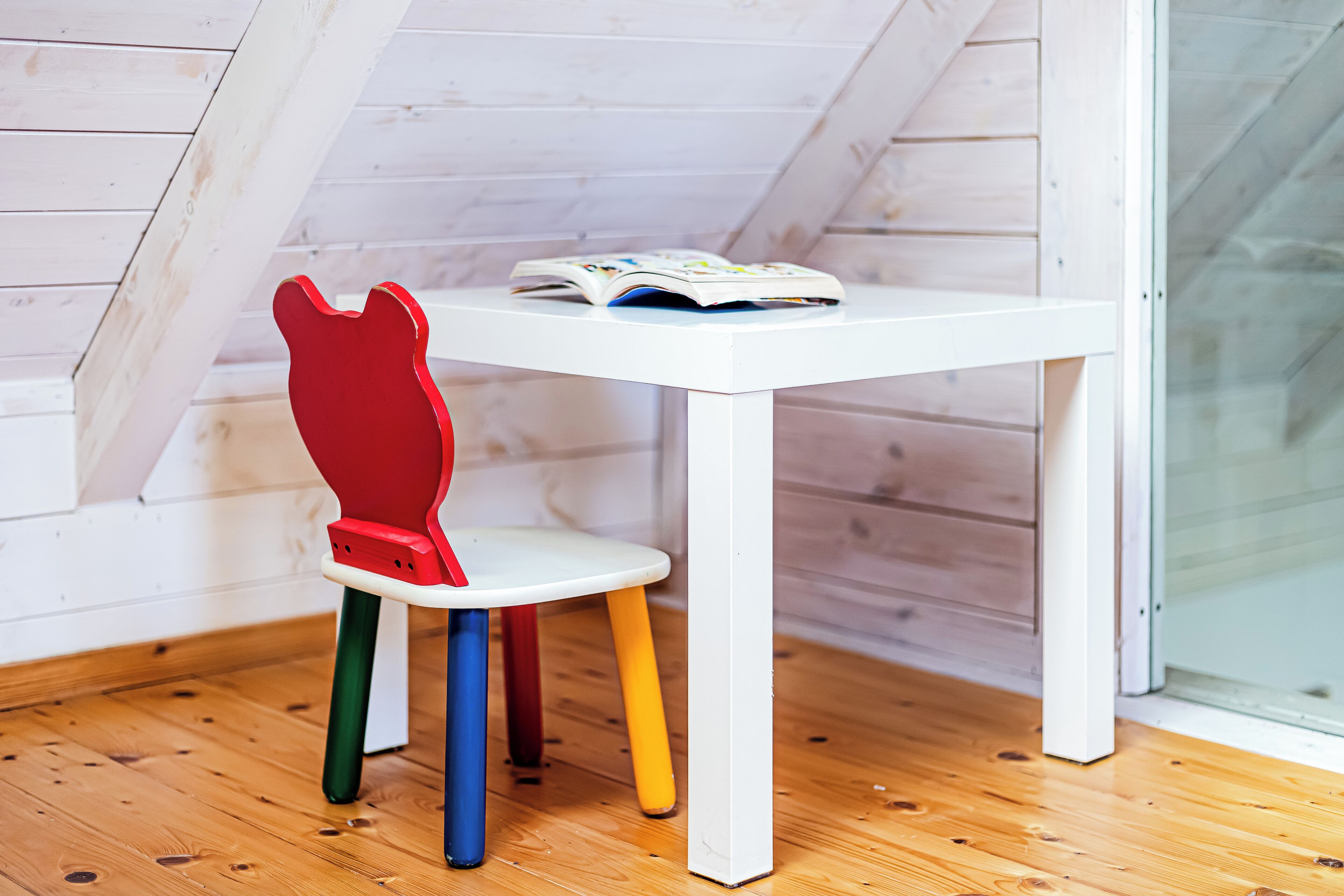 A white table with a colorful chair in a room with wooden floors and white walls.