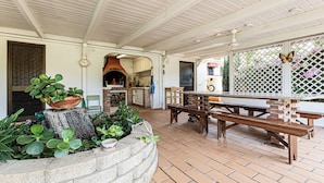 Un espace extérieur aménagé en terrasse, avec un sol en briques, des bancs en bois, une cheminée en briques et une table en bois.