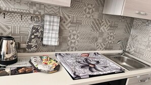 Et køkken med et mønstret bagpanel, en elkedel, en bakke med mad og en vask.
