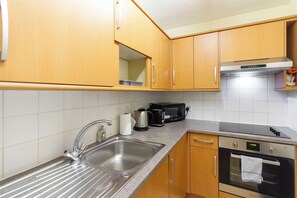 A kitchen with a stainless steel sink, a kettle, a toaster, a microwave, and an oven.