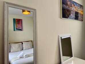 A hotel room with a bed, a mirror, a painting, and a light fixture.
