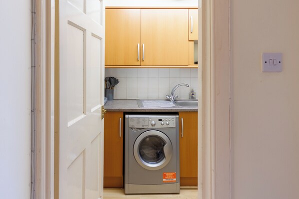 A compact kitchen with wooden cabinets, a washing machine, and a sink.