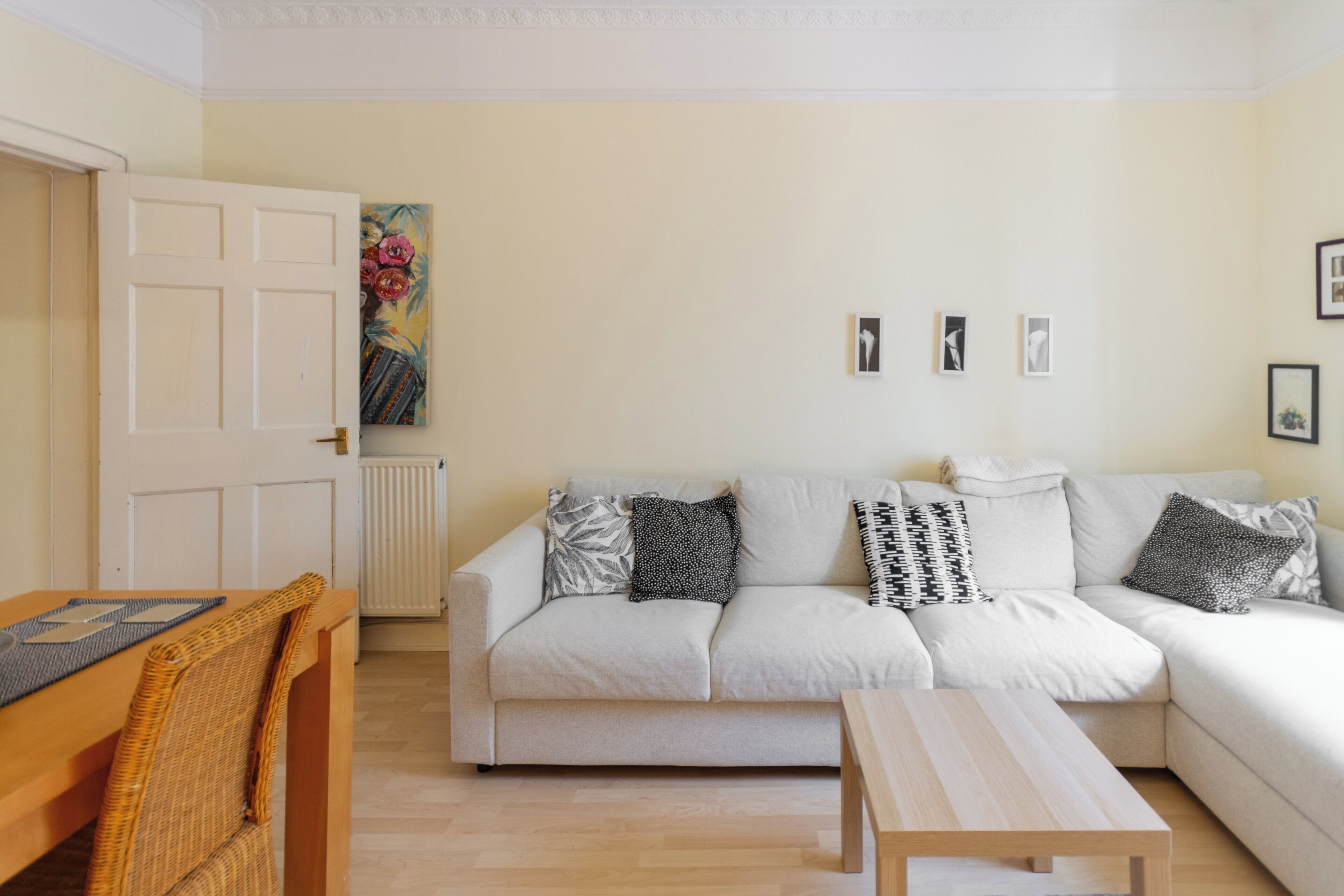 Uma sala de estar com sofá, mesa de madeira, cadeira de vime e radiador.