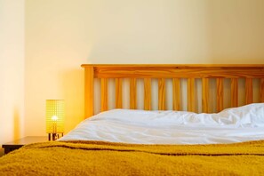 A bed with white linens, a wooden headboard, and a yellow blanket.