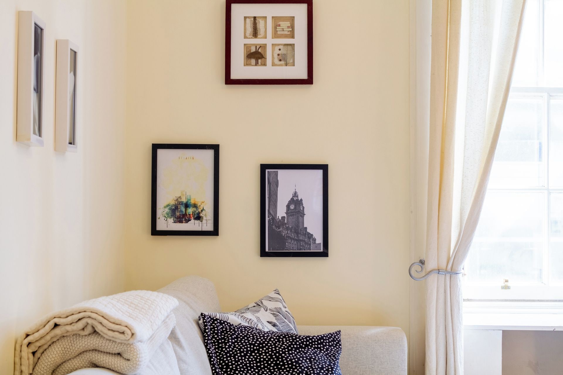 A room with a sofa, a window with curtains, and three framed pictures on the wall.