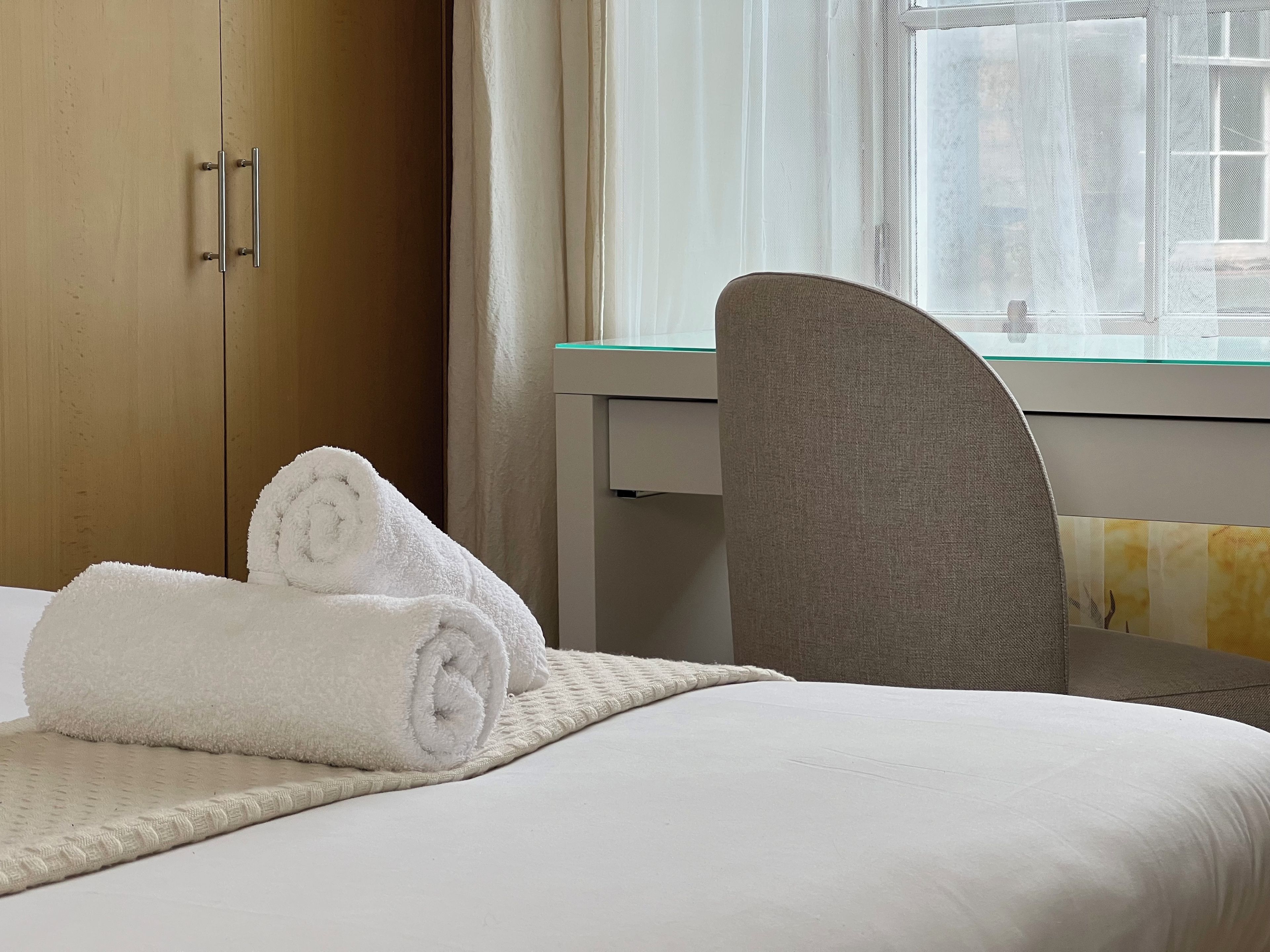 A hotel room with a bed, a chair, a desk, and a window.