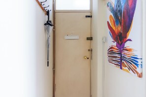 A beige door with a small sign, a coat rack with a closed umbrella, and a colorful abstract painting on the wall.