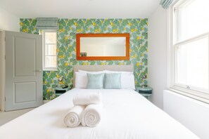 Una camera d'albergo con un letto, un comodino, uno specchio e una finestra.