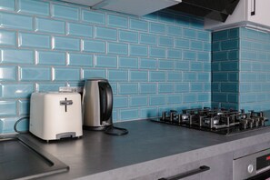 A kitchen with a blue tiled backsplash, a toaster, a kettle, and a gas stove.