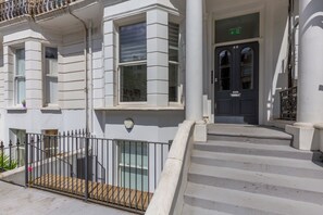 A building with a white facade, a black door with the number 68, and a small balcony with a metal railing.