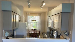 A modern kitchen with a central island, white cabinetry, and a dining area with a wooden table and white chairs.