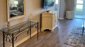 A living room with a large mirror, a flat-screen TV, a glass coffee table, and a wooden cabinet.