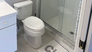 A bathroom with a toilet, a glass-enclosed shower, and a framed picture on the wall.
