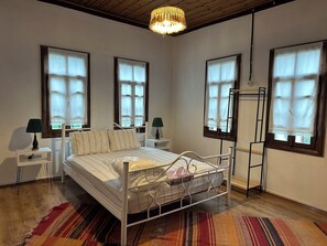 Een slaapkamer met een metalen bedframe, twee nachtkastjes met lampen, een raam met gordijn en een houten trap.