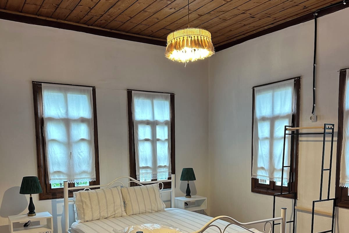 Une chambre à coucher avec un lit, deux tables de chevet, une lampe, une fenêtre et un plafond en bois.