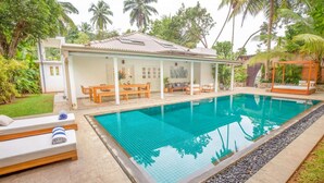 Un espace aménagé au bord de la piscine, comprenant un coin salon couvert, des chaises longues et une piscine.