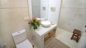 Une salle de bain équipée d’un WC, d’un lavabo, d’un miroir, d’une douche et d’un petit tabouret.