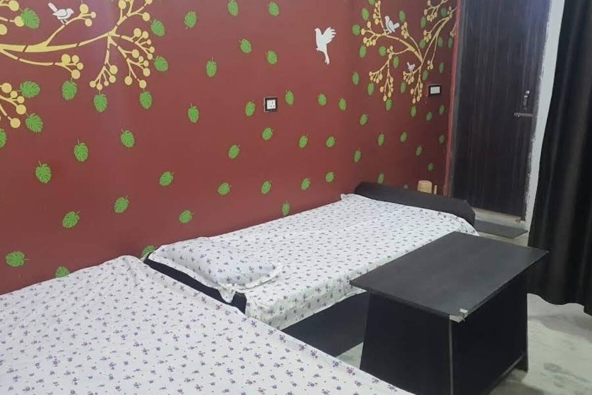 A room with two beds, a red wall with green leaf patterns, and a door with a curtain.