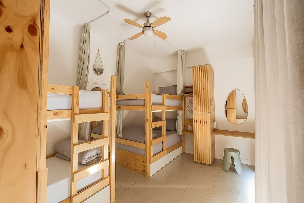 Une chambre avec des lits superposés, un ventilateur de plafond, un miroir et une petite poubelle.