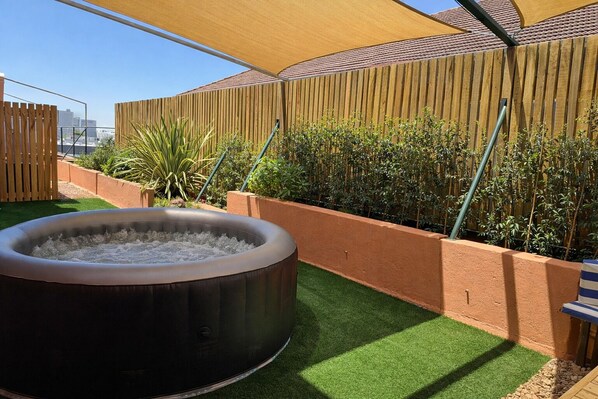 A hot tub in a landscaped outdoor area with artificial grass, wooden fencing, and a variety of plants. - Sweet Stay (Cape Town)