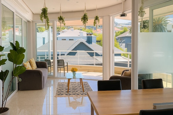 A spacious living area with a sofa, chairs, a coffee table, and a view of the neighborhood through large windows.