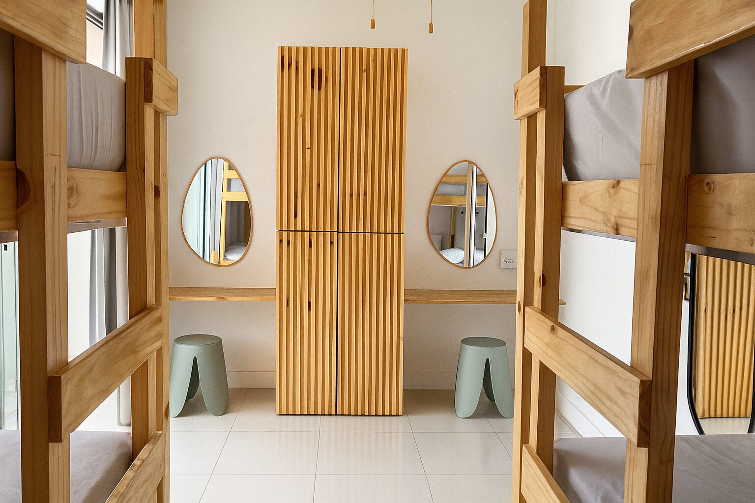 Una habitación con una cama litera, un separador de listones de madera, dos espejos redondos y un piso de tonos claros.