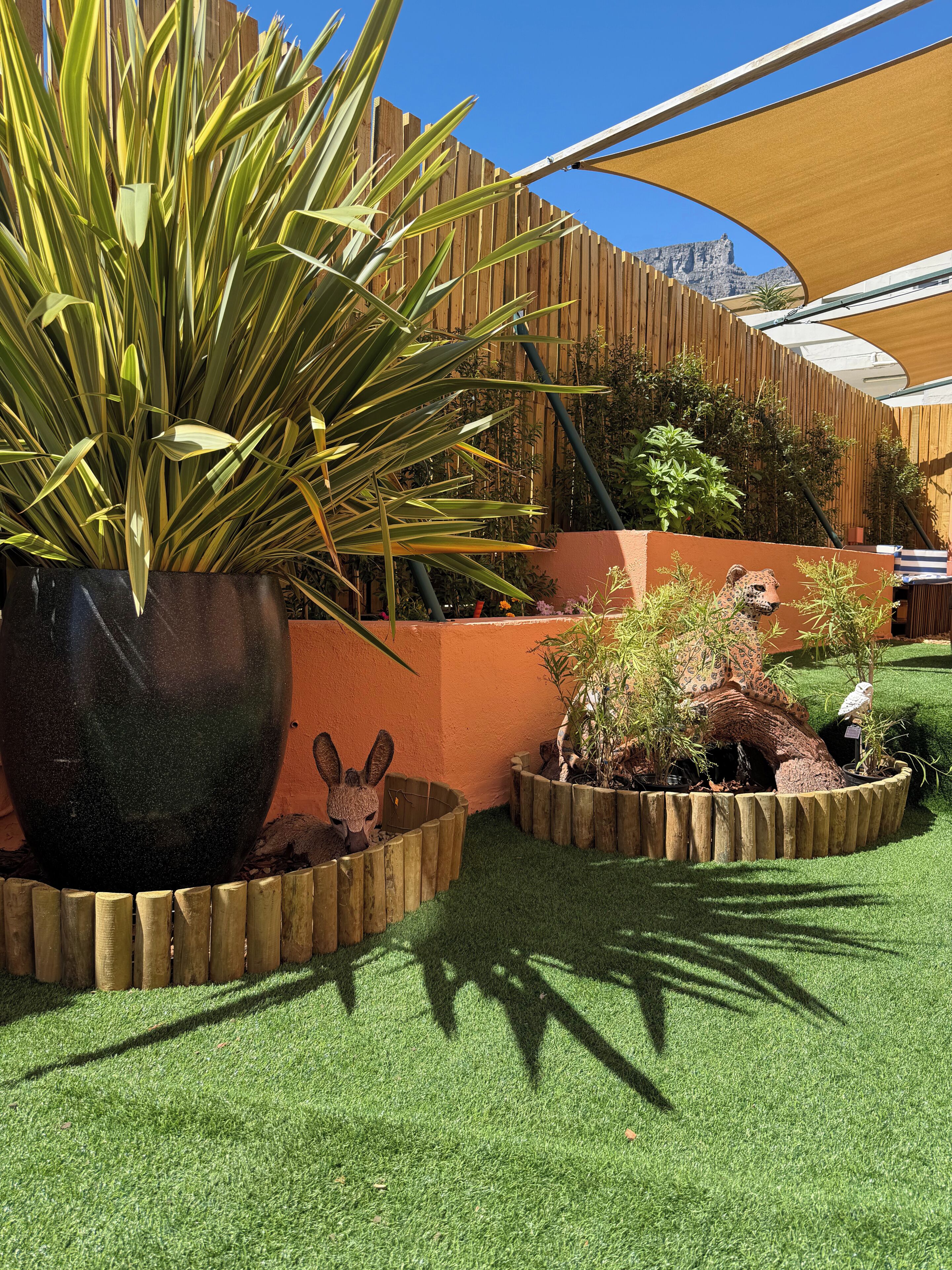 A garden with a large potted plant, a wooden fence, and a small animal figurine.