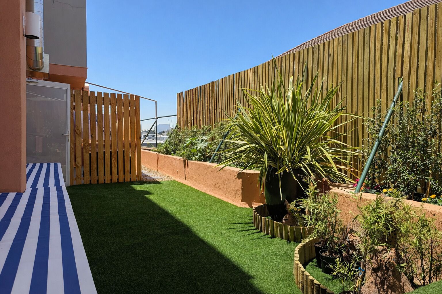 Un patio con césped artificial, valla de madera y plantas en macetas.