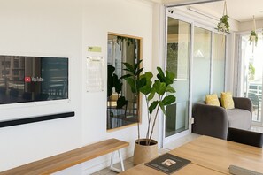 A modern room with a wooden bench, a potted plant, a table with a magazine, and a YouTube sign on the wall. - Sweet Stay (Cape Town)