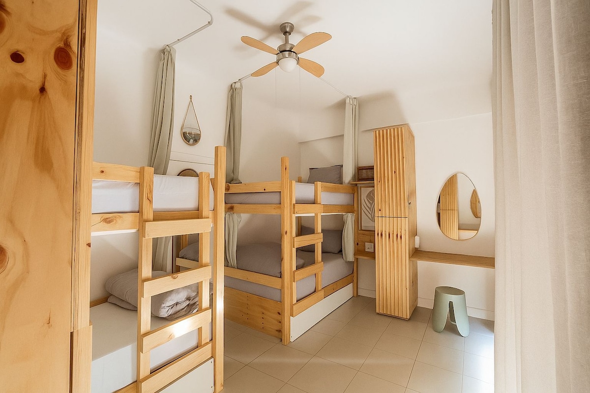 A room with bunk beds, a ceiling fan, a mirror, and a small trash bin.