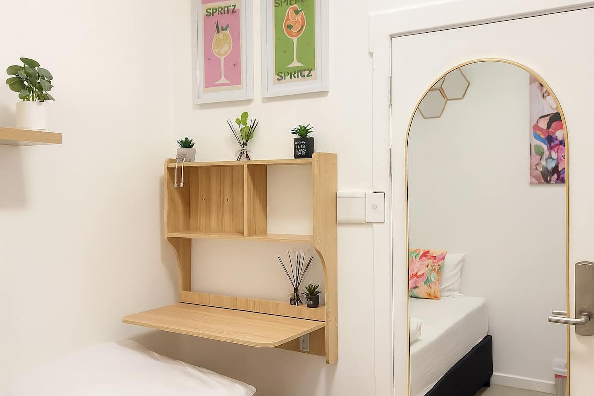 Une chambre à coucher comprenant un lit, une étagère en bois, un miroir et deux tableaux accrochés au mur.