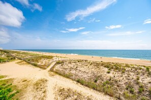 Une plage avec un sentier sablonneux et des dunes, qui mène à l’océan.