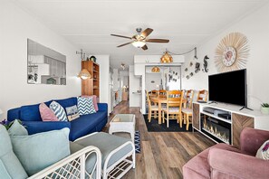 Ein modernes Wohnzimmer mit einem blauen Sofa, einem pinken Sessel, einem Fernseher und einem Kamin.