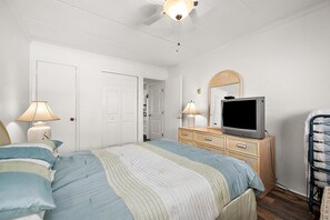 Une chambre à coucher comprenant un lit, une commode, un téléviseur et un ventilateur de plafond.