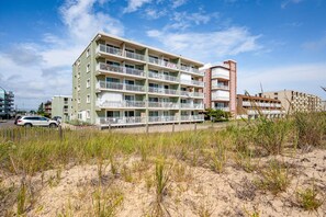 Un immeuble à plusieurs étages doté de balcons, avec un premier plan sablonneux et un ciel dégagé.