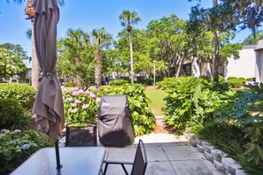 Une terrasse avec une table et des chaises, entourée d’une végétation luxuriante et de différentes espèces de plantes.