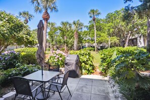 Une terrasse extérieure avec une table et des chaises, entourée d’une végétation luxuriante et de palmiers.