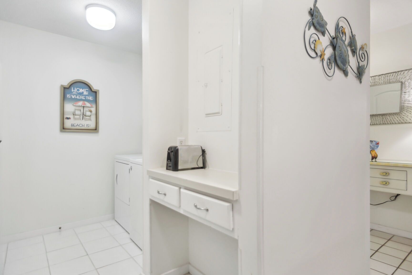 Une salle de bain propre et blanche, avec un porte-serviettes, un petit plan de travail sur lequel se trouve un grille-pain, et un miroir fixé au mur.
