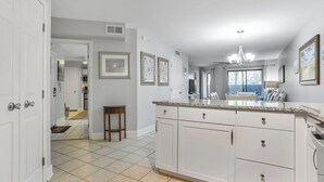 A kitchen with white cabinets, a granite countertop, and a dining area with a table and chairs. - First Floor Two Bedroom Two Bath Condo - 1 Block to Beach (Hilton Head Island)