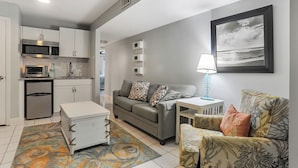 A modern apartment with a kitchenette, a grey sofa, a patterned armchair, a small side table with a lamp, and a framed picture on the wall. - First Floor Two Bedroom Two Bath Condo - 1 Block to Beach (Hilton Head Island)