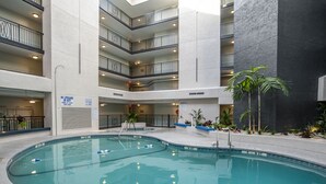 An indoor swimming pool with multiple levels of balconies, surrounded by plants and a stone wall. - First Floor Two Bedroom Two Bath Condo - 1 Block to Beach (Hilton Head Island)