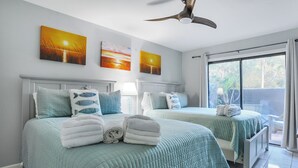 A hotel room with two beds, each with a teal bedspread and matching pillows, a ceiling fan, and artwork depicting sunsets. - First Floor Two Bedroom Two Bath Condo - 1 Block to Beach (Hilton Head Island)